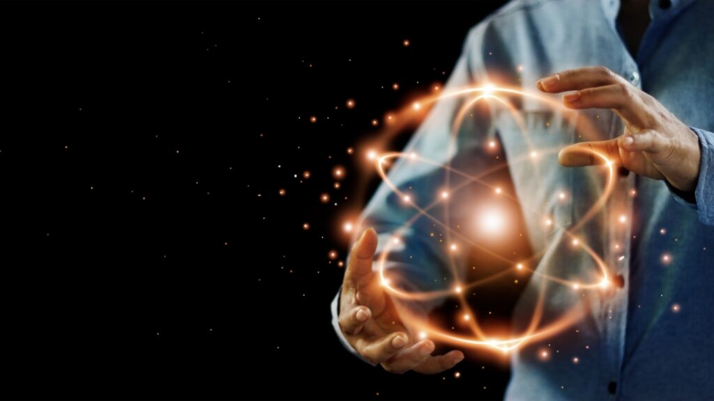 抽象的な科学、暗い背景上の原子粒子、核エネルギーのイメージとネットワーク接続を持つ手。