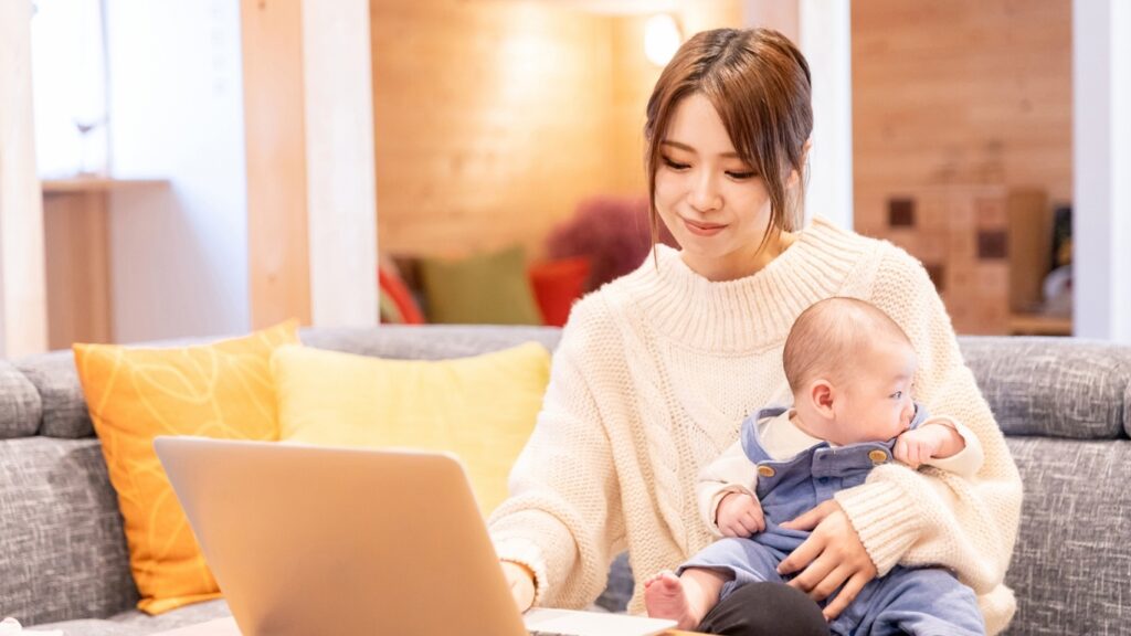 赤ちゃんを抱いてリモートワークする若い母親