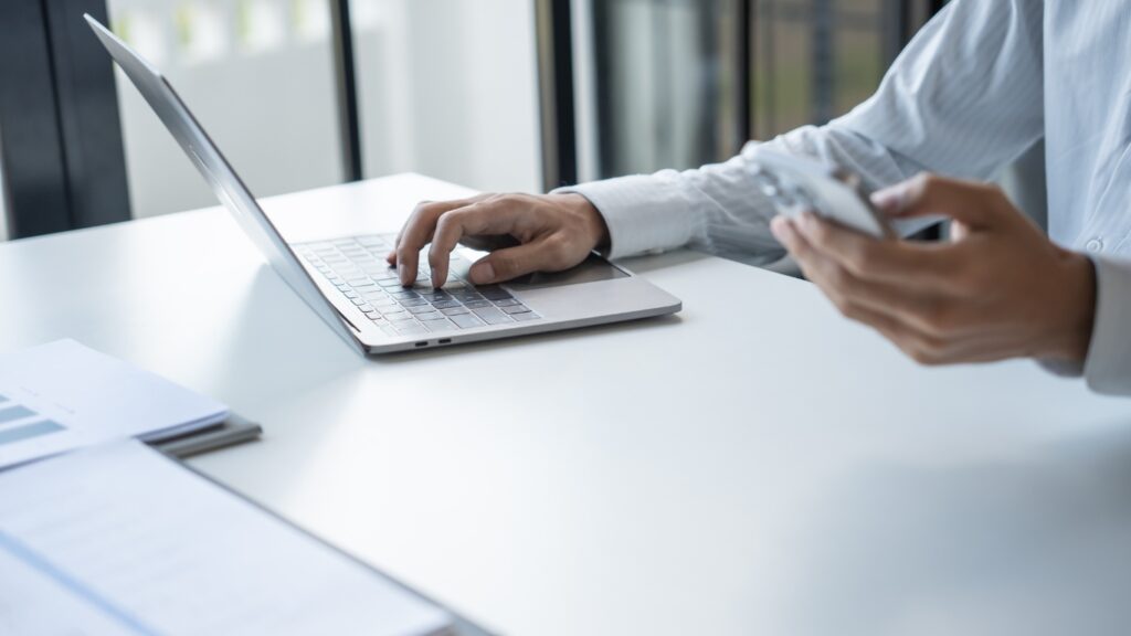 ノートパソコンとスマホで作業するビジネスパーソン